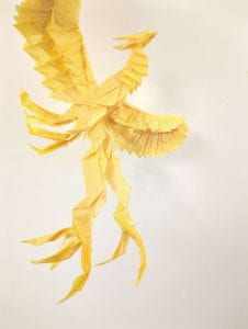 an origami piece of a yellow phoenix in flight